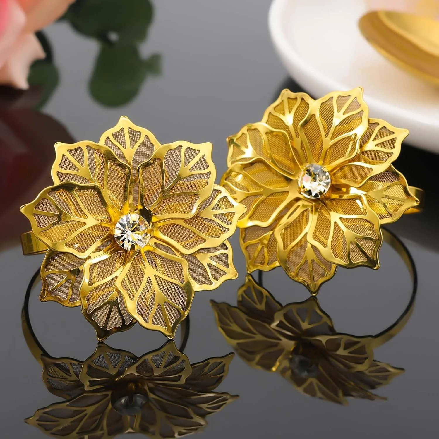 Gold floral earrings with diamond center stones reflected on a shiny black surface.