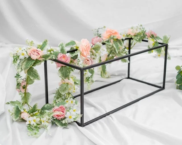 Black metal frame adorned with pink and white flowers and green leaves on a light fabric background.
