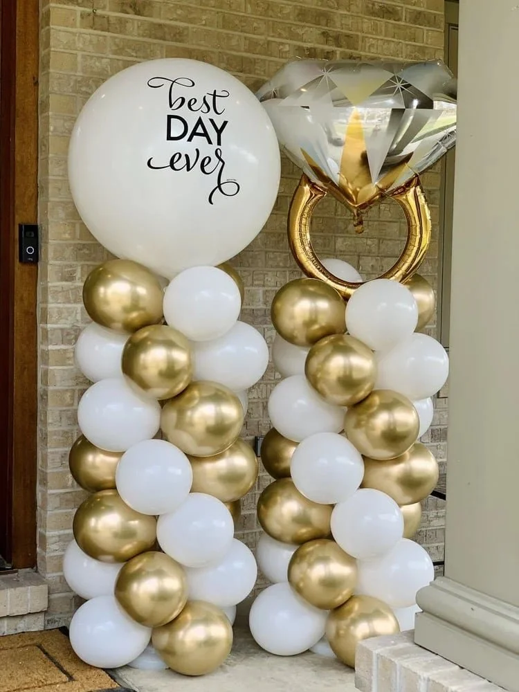 Decorative balloon arrangements with white, gold, and metallic silver balloons, including a large white balloon with the message "Best Day Ever" and a diamond-shaped metallic silver balloon on top of a circular gold frame.