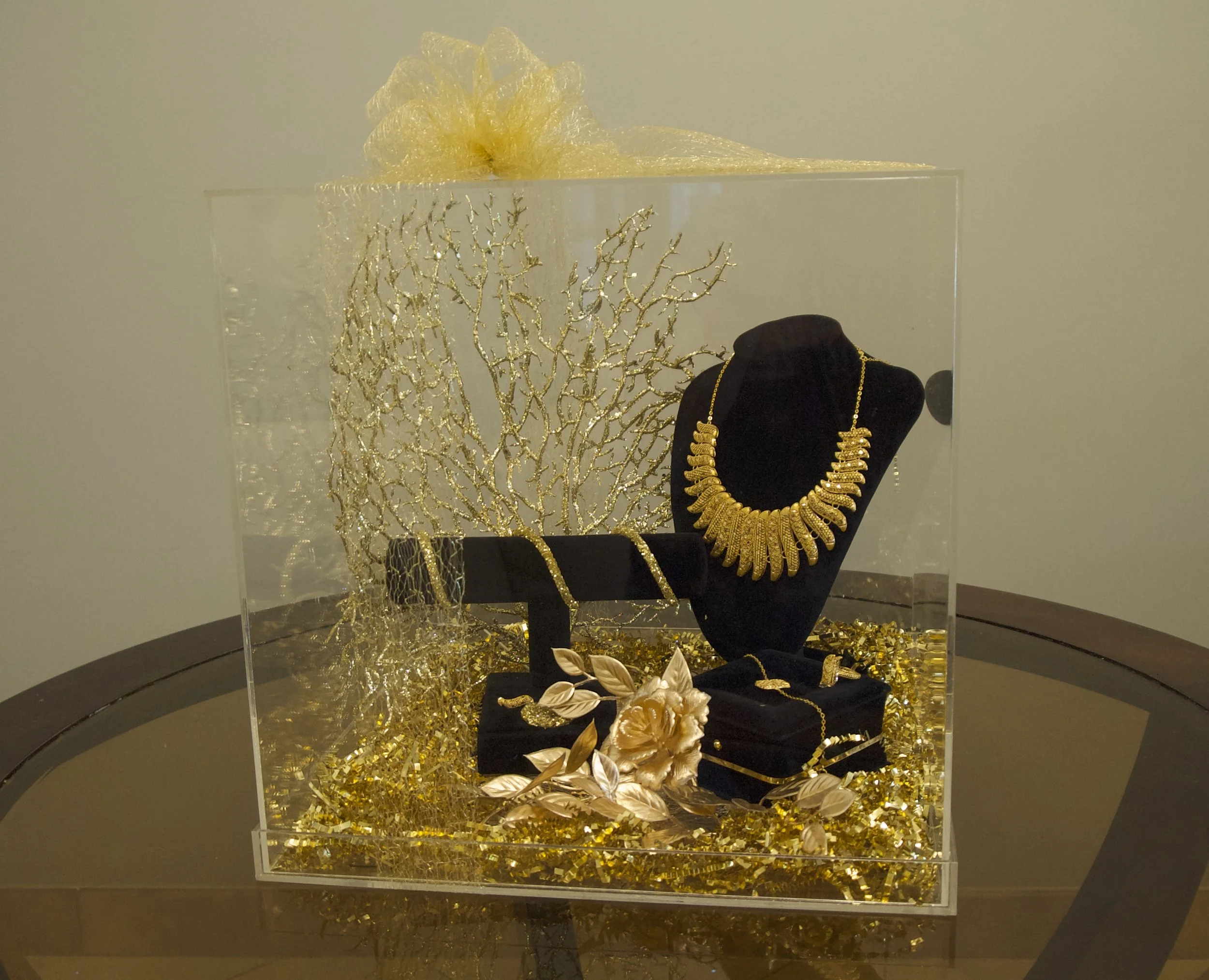 Gold necklace and jewelry set displayed elegantly in a transparent box with decorative gold accents and a bow on top.