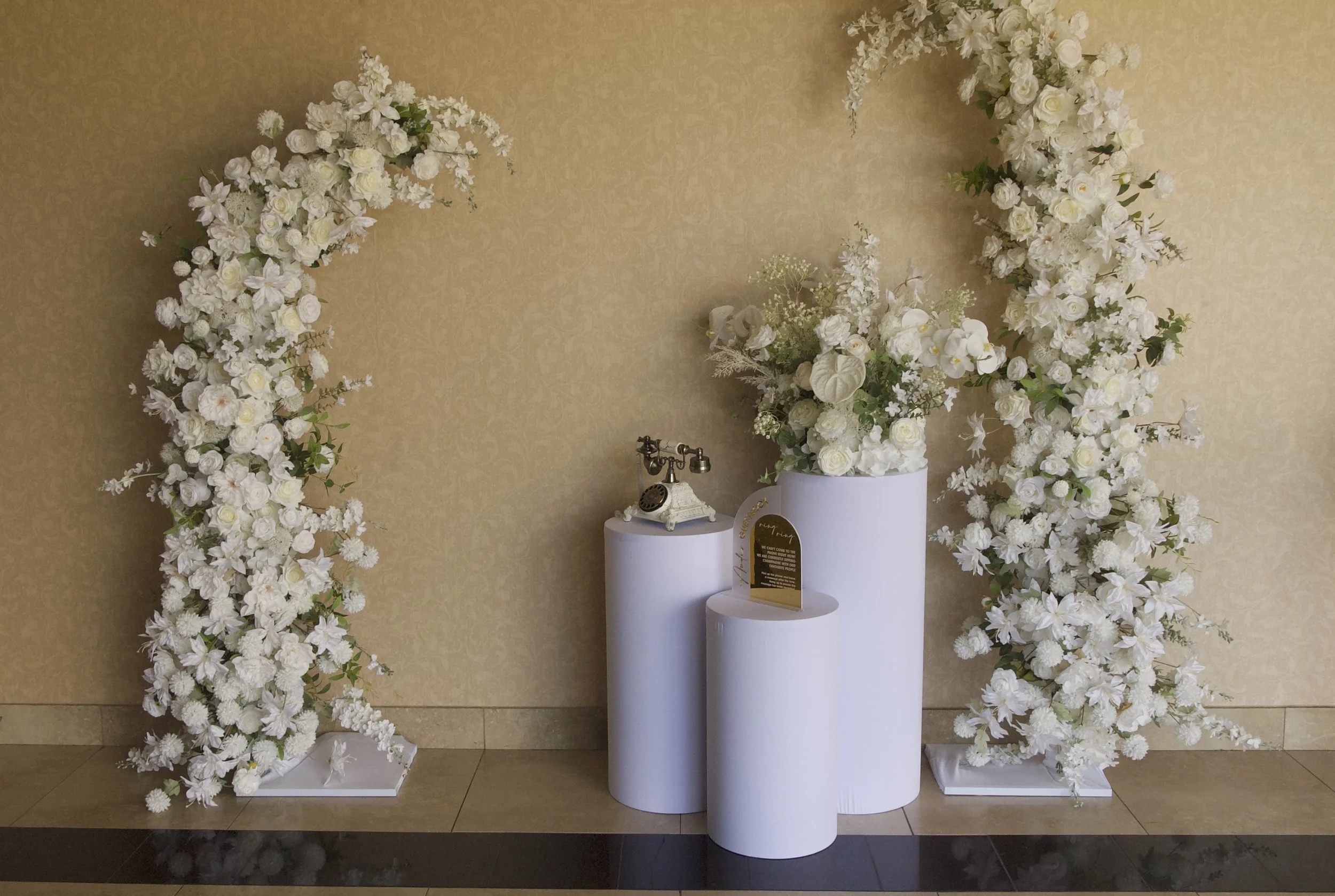 Elegant floral display with lush white flowers on tall white pillars and an antique telephone.