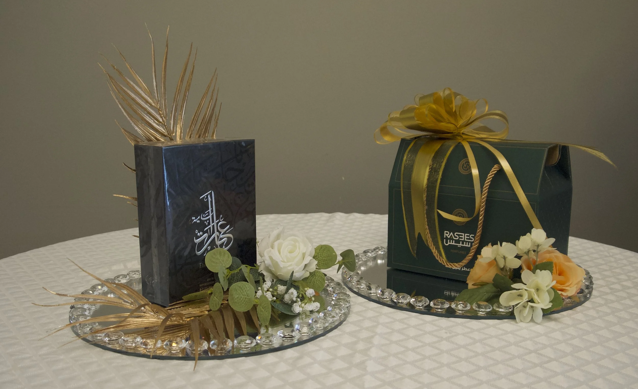 Two elegant gift boxes on a table, one with Arabic script and a gold decorative leaf, and the other with a gold ribbon and floral accents.